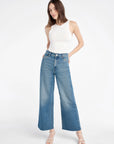 Woman wearing a white sleeveless top and blue jeans on a white background full body view