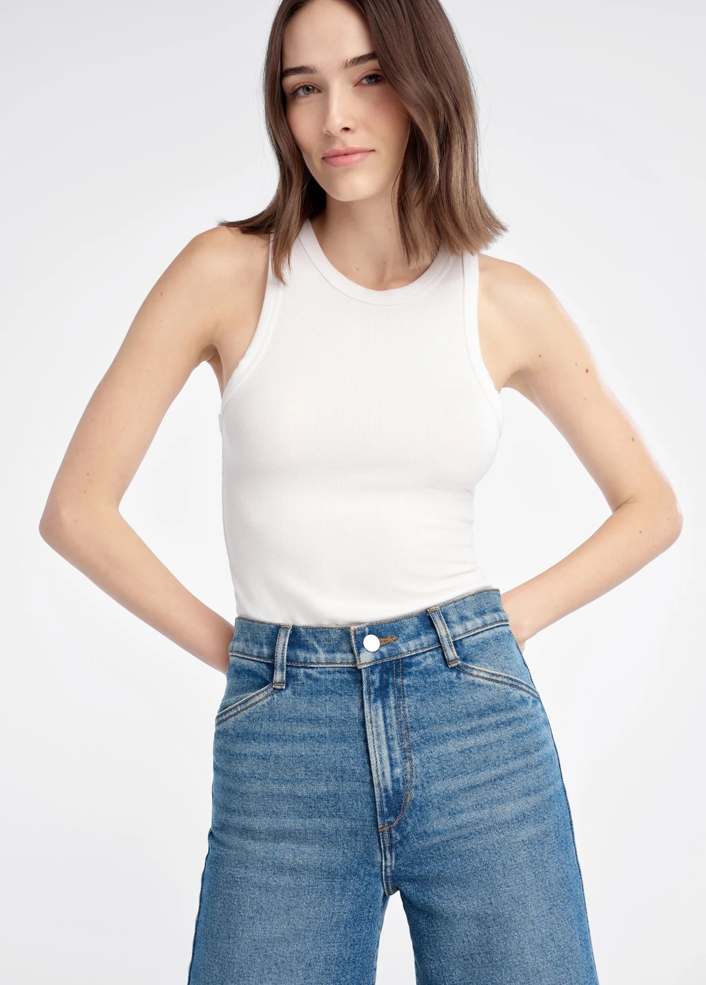 Woman wearing a white tank top and blue jeans on a white background