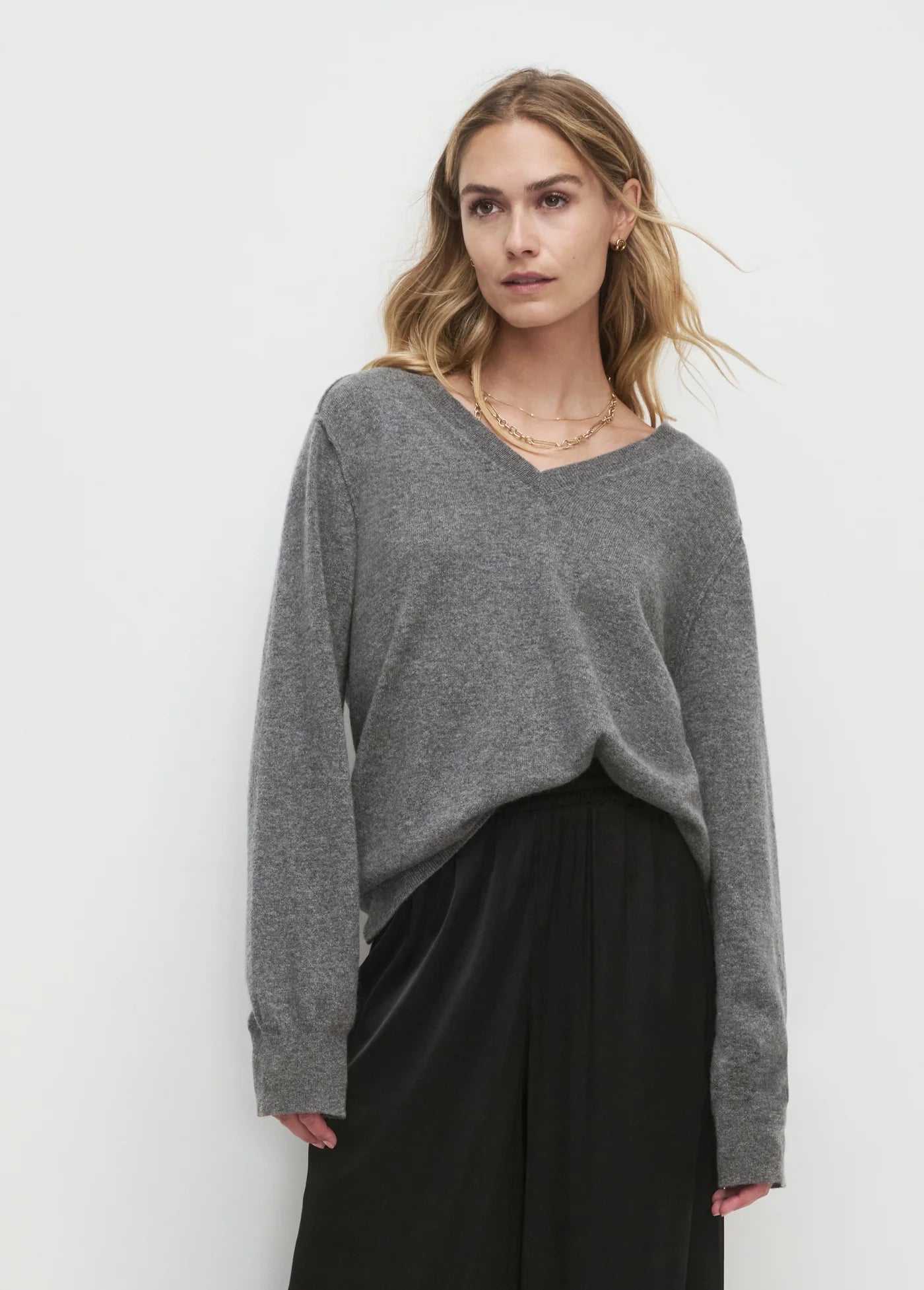 Woman wearing a gray sweater and black pants against a white background