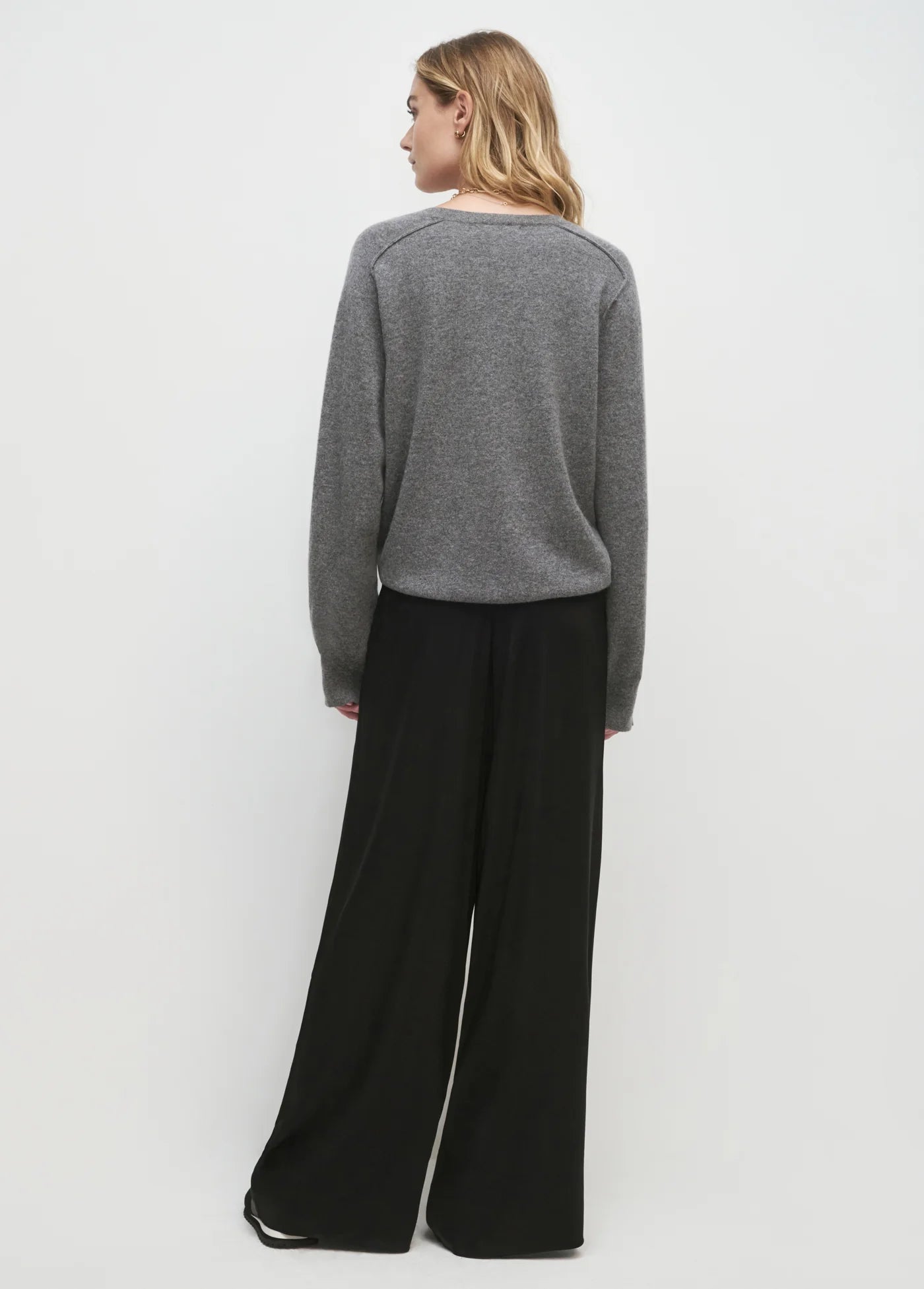 Person wearing a gray sweater and black pants on a white background