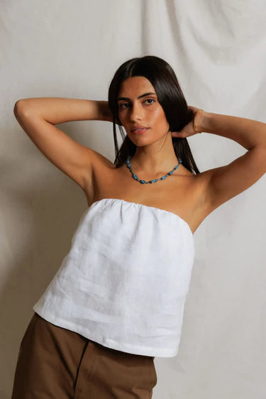 Woman wearing a white strapless top and brown pants against a plain background