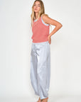 A woman modeling a sleeveless red and white striped top paired with shiny light silver wide-leg pants and beige sandals, standing against a plain white studio background.