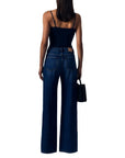 A woman shown from the back wearing a dark navy camisole top and high-waisted dark blue wide-leg jeans, holding a small black handbag against a plain white background.