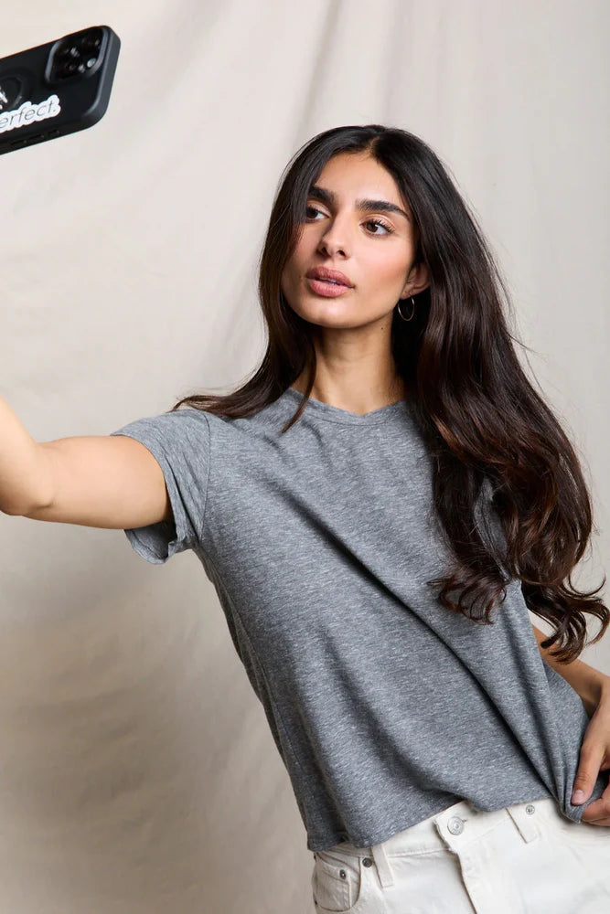 Woman taking a selfie wearing a gray t-shirt against a plain background