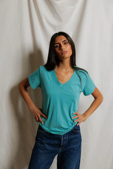 model wearing a teal tee with jeans on a cream background