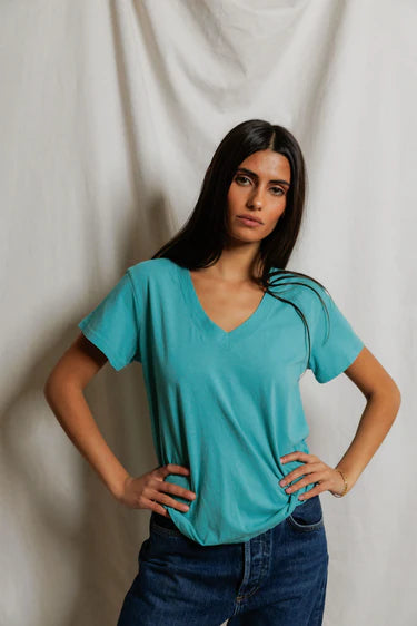model wearing a teal tee with jeans on a cream background
