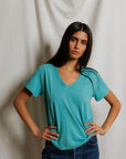 model wearing a teal tee with jeans on a cream background