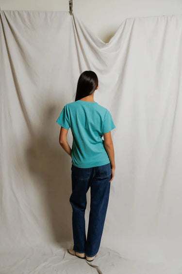 model wearing a teal tee with jeans on a cream background, back