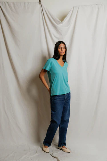 model wearing a teal tee with jeans on a cream background