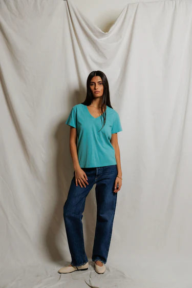 model wearing a teal tee with jeans on a cream background