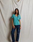model wearing a teal tee with jeans on a cream background