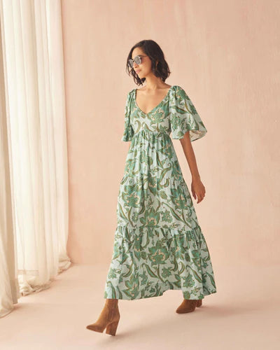 Woman wearing a green floral dress against a light pink background