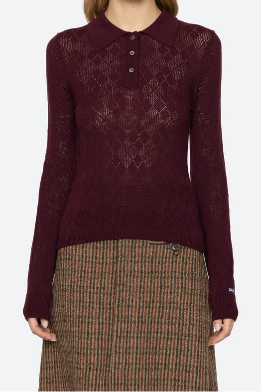 Woman wearing a burgundy patterned shirt and plaid skirt on a white background