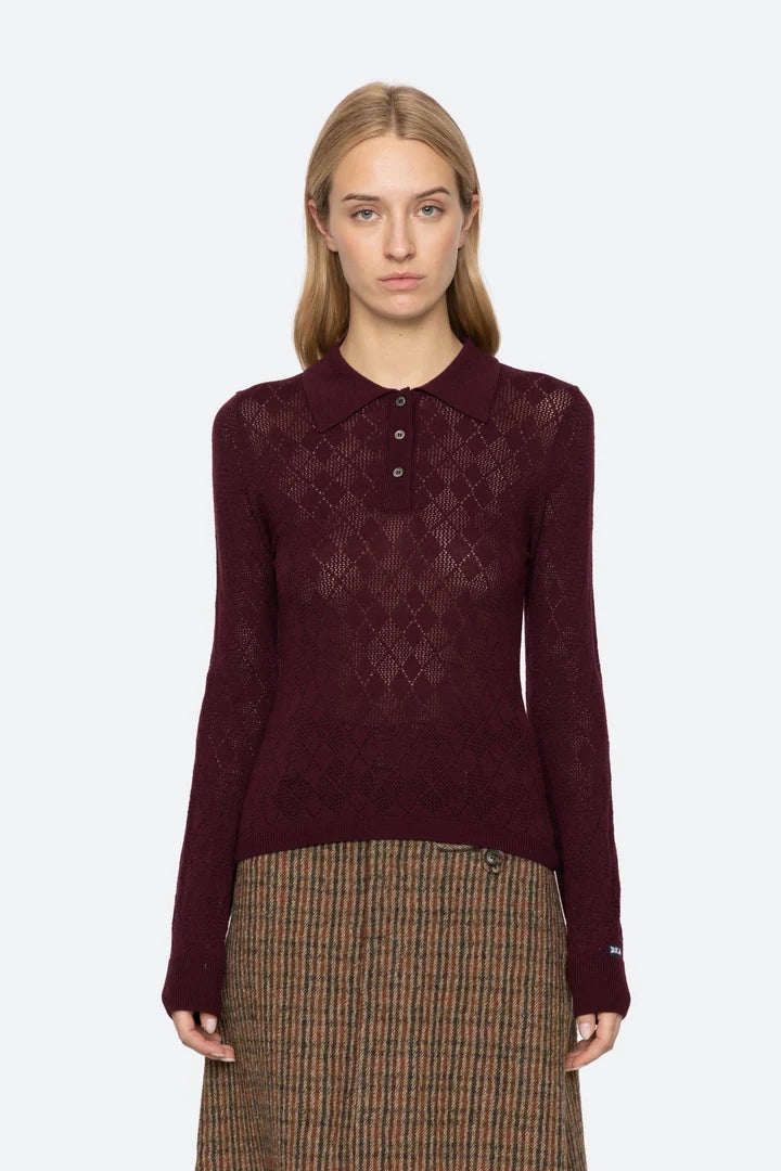 Woman wearing a burgundy patterned shirt and plaid skirt on a white background