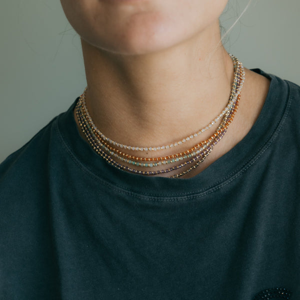Person wearing a stack of beaded necklaces on a plain background