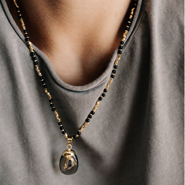 Necklace with black beads and gold accents worn by a person in a gray shirt.