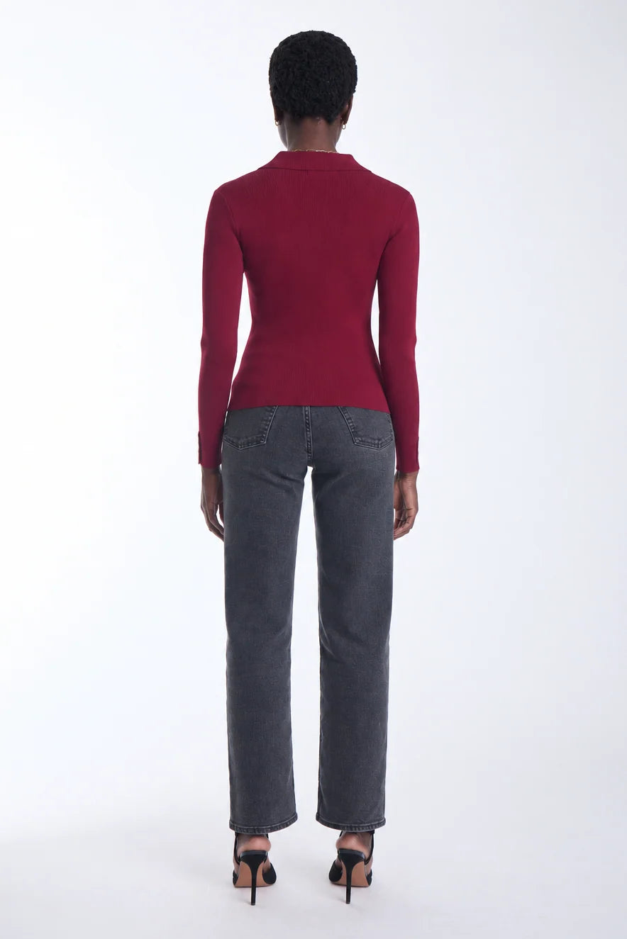 A model shown from the back wearing a fitted burgundy long-sleeve top, dark gray straight-leg jeans, and black high-heeled sandals against a plain white studio background.