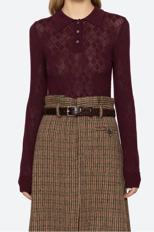 Woman wearing a burgundy patterned shirt and plaid skirt on a white background