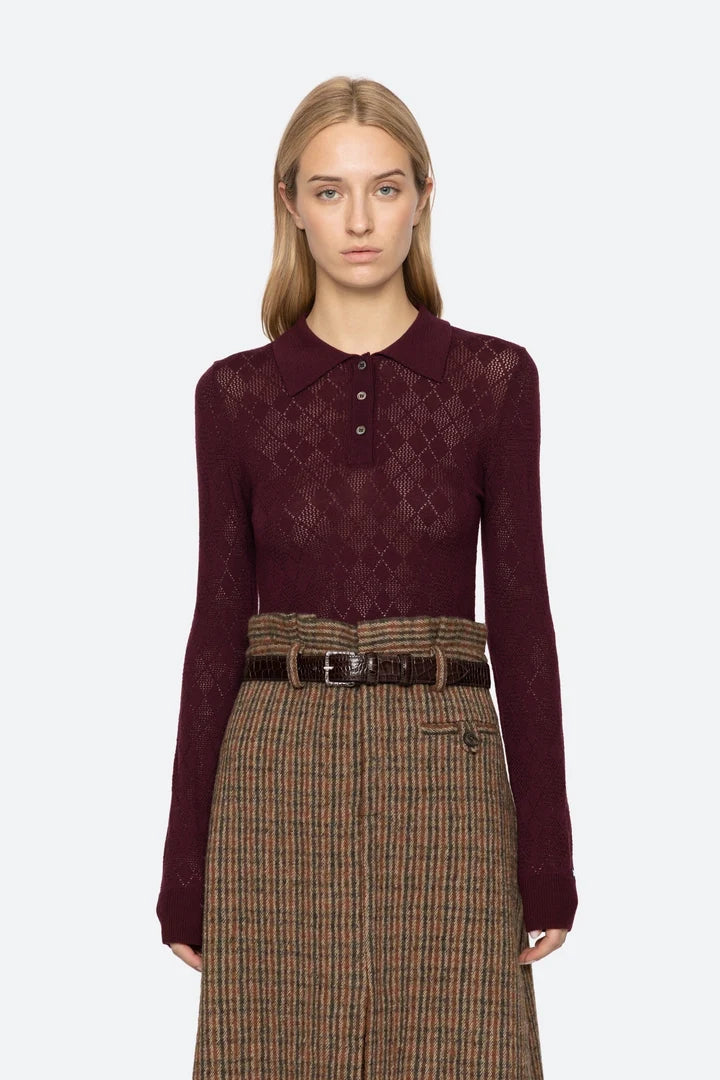 Woman wearing a burgundy patterned shirt and plaid skirt on a white background
