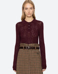 Woman wearing a burgundy patterned shirt and plaid skirt on a white background