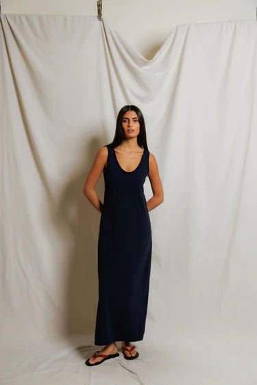 Woman wearing a navy blue dress standing against a plain white curtain.