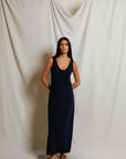 Woman wearing a navy blue dress standing against a plain white curtain.