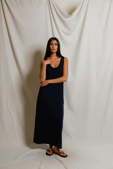 Woman wearing a navy blue dress standing against a plain white curtain.