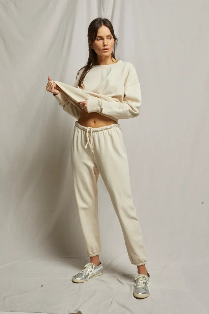 Woman wearing a beige sweatshirt and pants with sneakers on a plain background