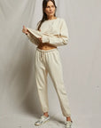 Woman wearing a beige sweatshirt and pants with sneakers on a plain background