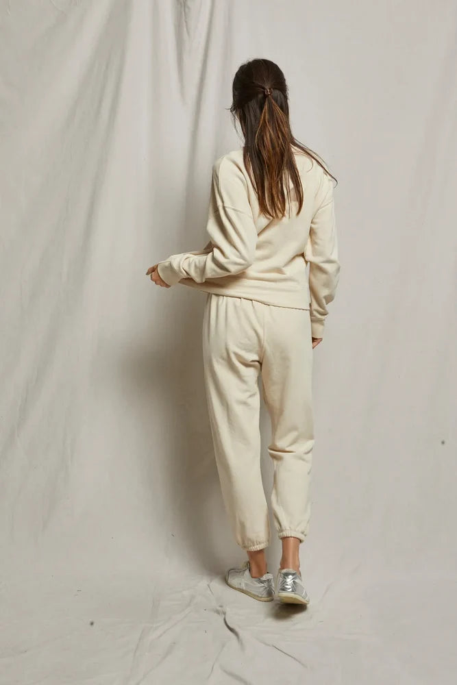 Person wearing a beige tracksuit standing against a plain background, back view