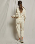 Person wearing a beige tracksuit standing against a plain background, back view