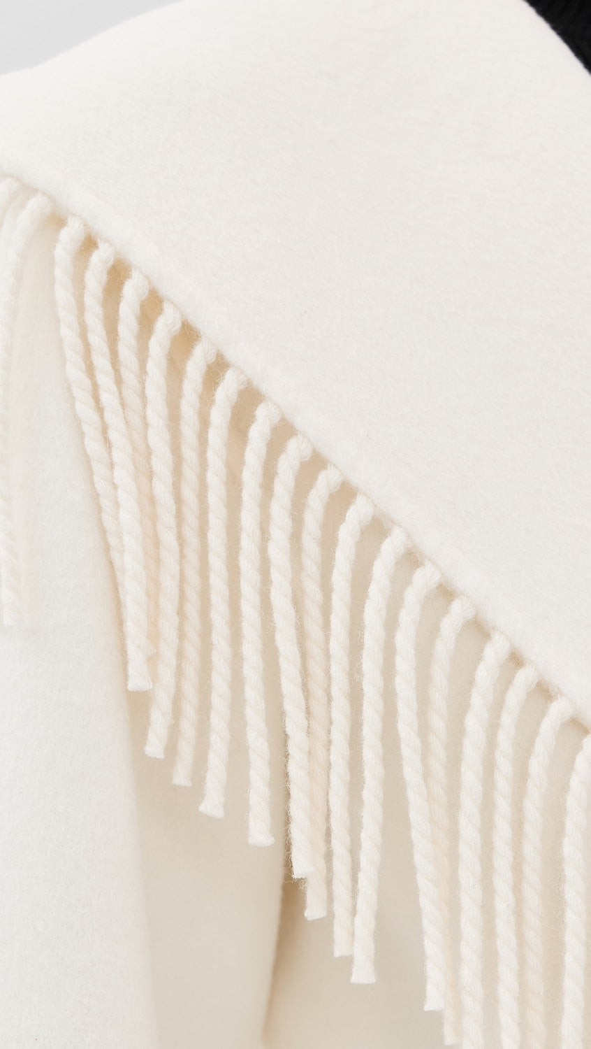 Close-up of a cream-colored knit fabric with thick braided fringe tassels.