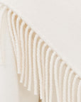 Close-up of a cream-colored knit fabric with thick braided fringe tassels.