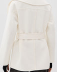 A woman shown from the back wearing a structured cream-colored coat with a wide collar and waist tie, paired with black pants and a black top underneath.