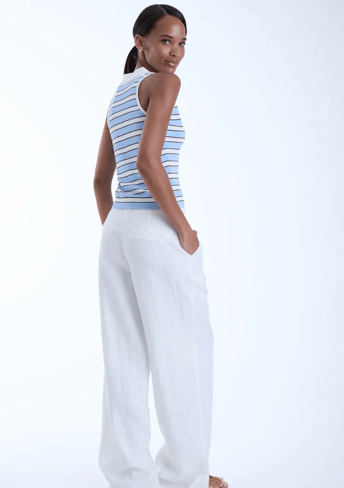 model wearing Kira sky sleeveless stripe top with white pants on a white background, back