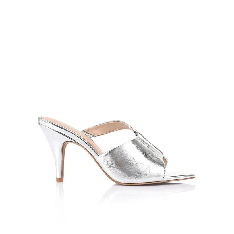 A single metallic silver mule sandal with a pointed toe, crisscrossing front straps, and a slim high heel, shown from a side profile on a white background.