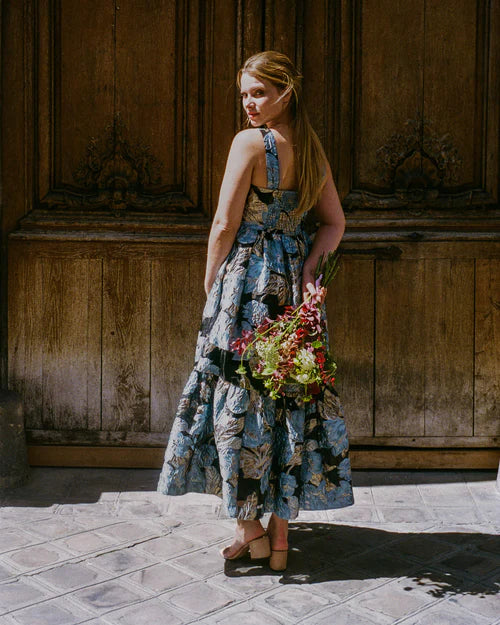 Woman in a floral dress holding flowers against a wooden door background