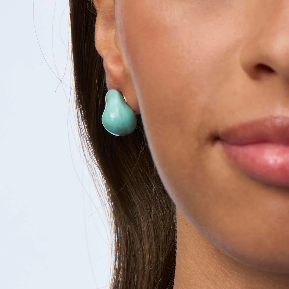 Close-up of a woman wearing turquoise earrings with a plain background