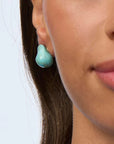 Close-up of a woman wearing turquoise earrings with a plain background