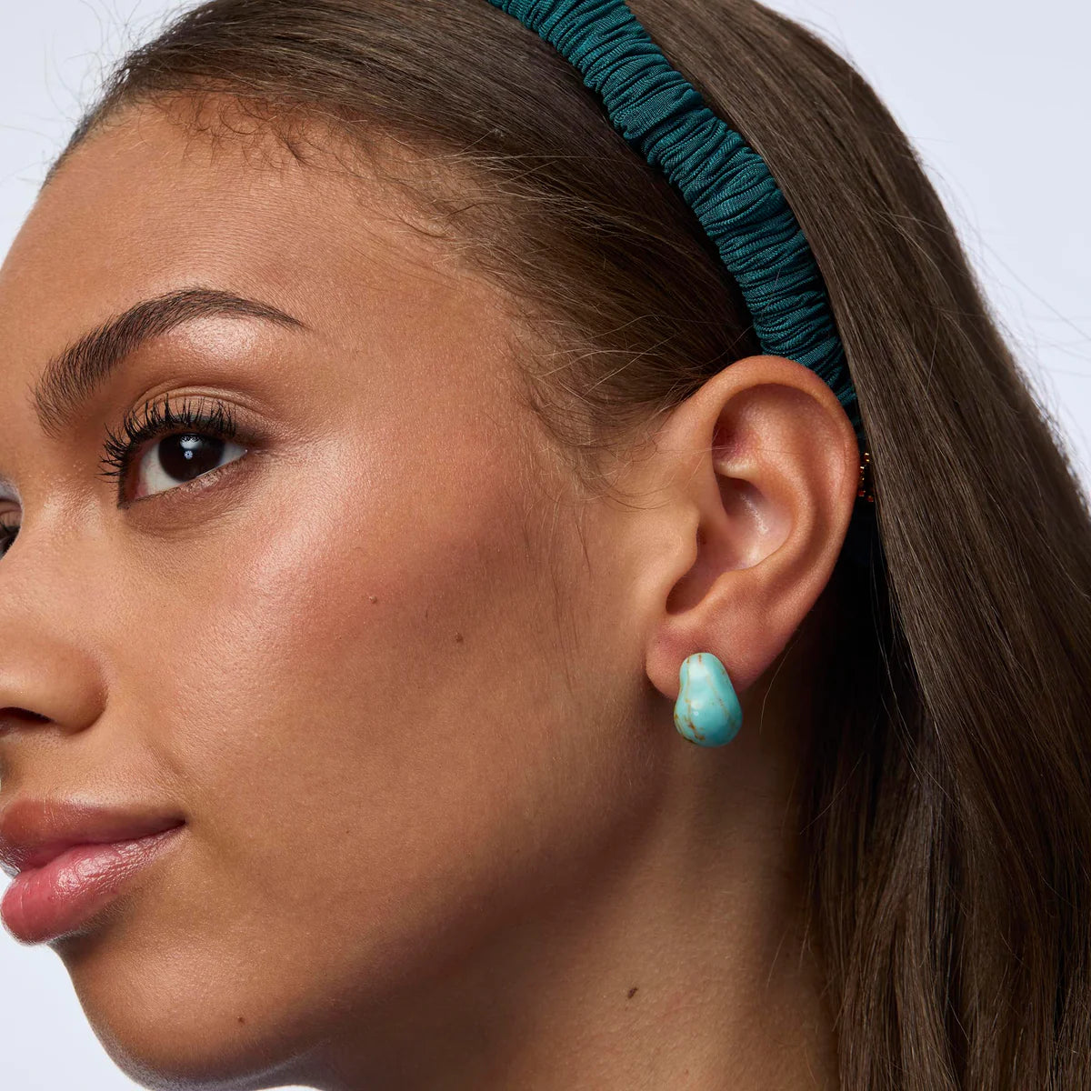 Close-up of a woman's face wearing turquoise earrings and headband.