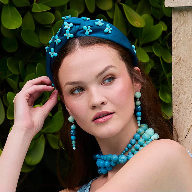 Woman wearing a blue headband and jewelry against a green leafy background