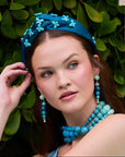 Woman wearing a blue headband and jewelry against a green leafy background
