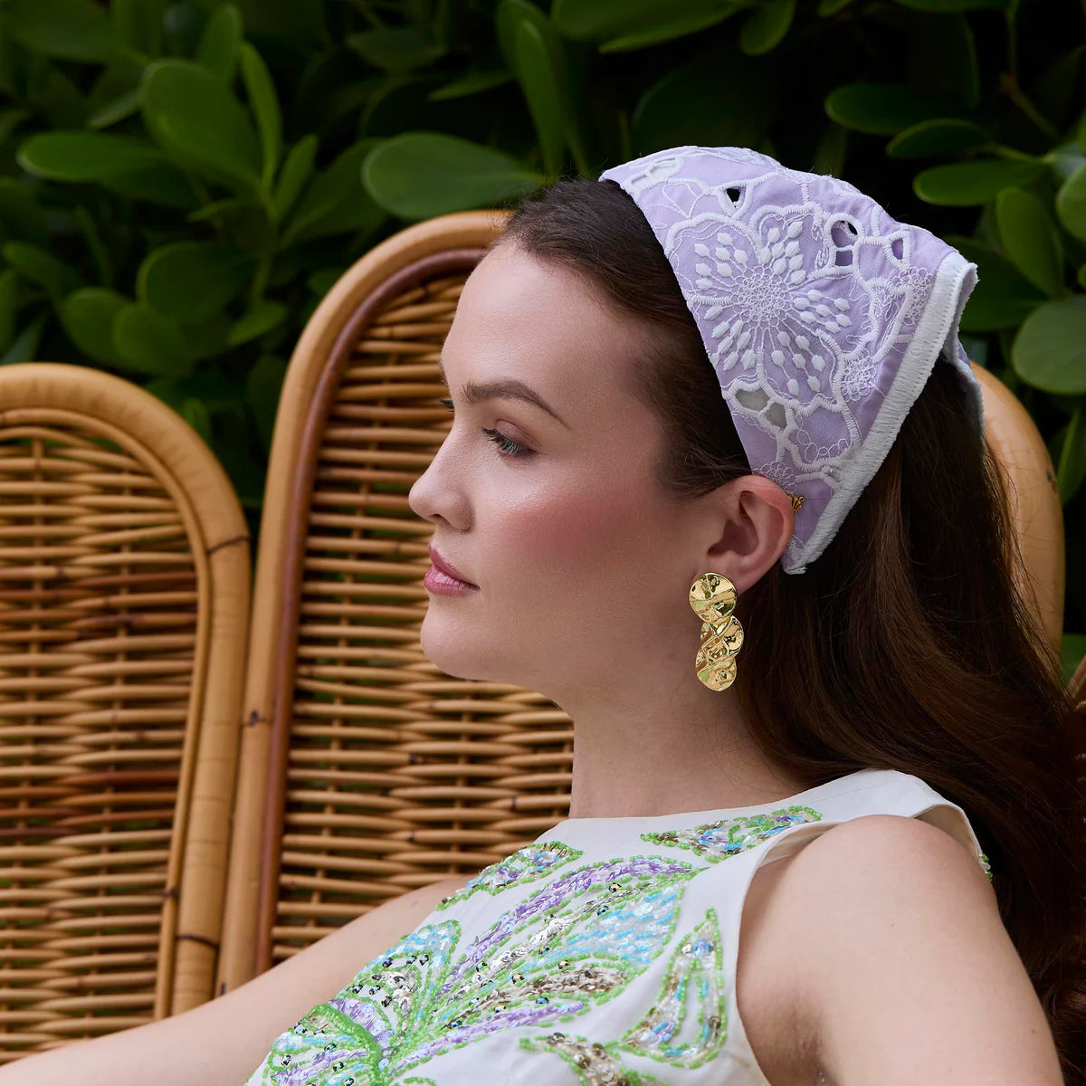 Woman wearing a decorative headband sitting on a wicker chair with greenery in the background