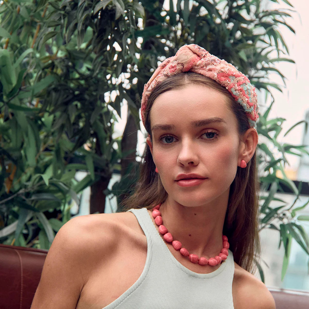 Woman wearing a pink headband and necklace with plants in the background