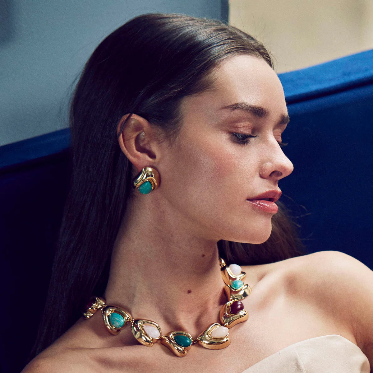 Woman wearing gold jewelry with turquoise stones against a blue background