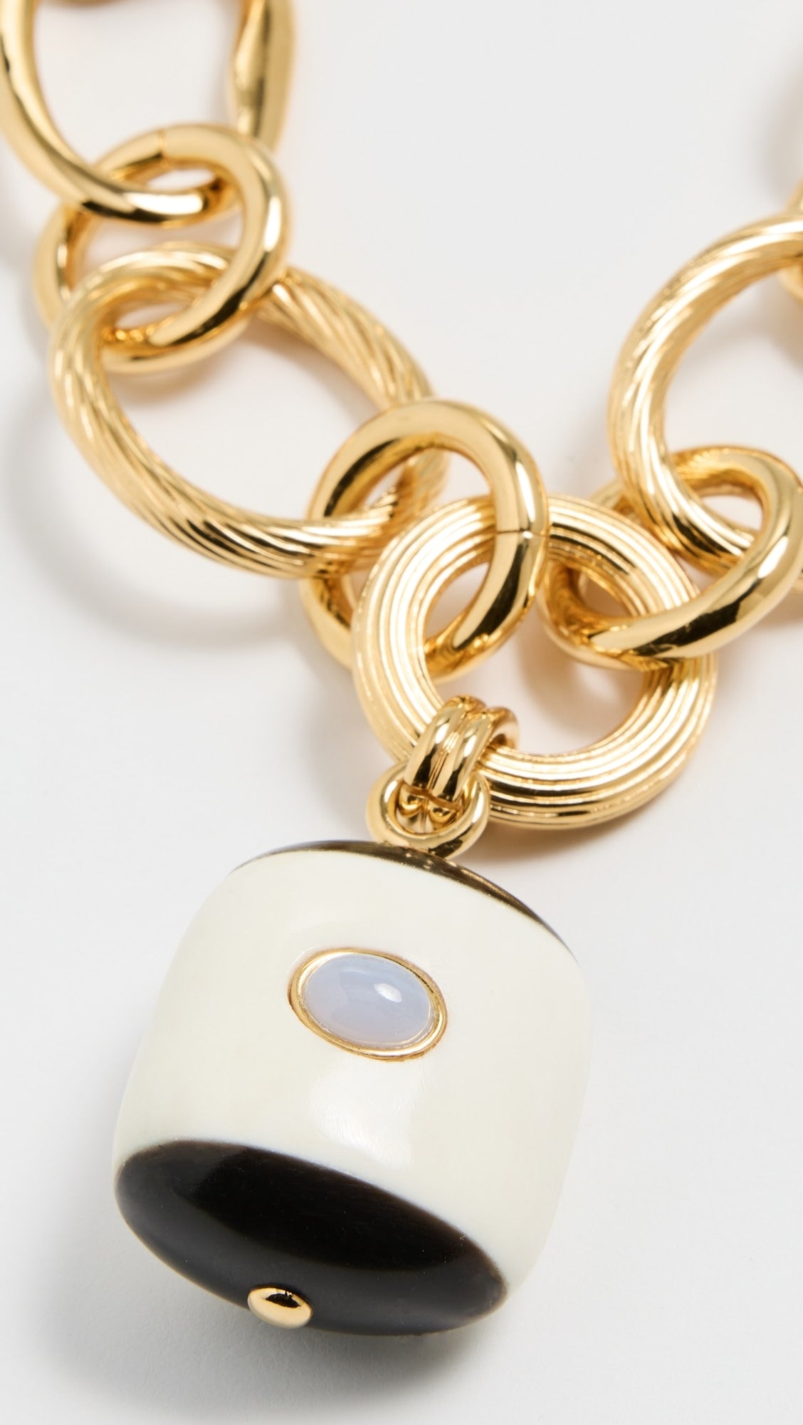 Gold chain with a white and black pendant on a light gray background