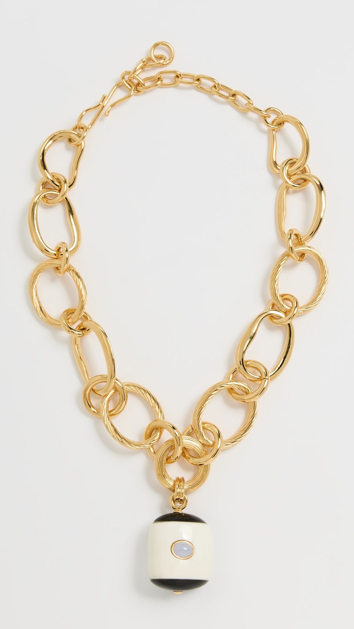 Gold chain bracelet with a black and white charm on a light gray background