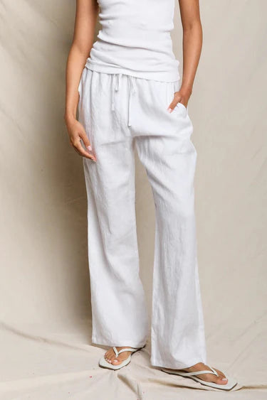 Person wearing white pants and a white top against a beige background