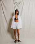 Woman wearing a white shirt and shorts with a black bralette against a plain background