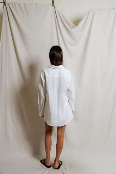 Person wearing a white shirt standing in front of a plain white curtain